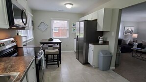 Una cocina equipada con estufa, microondas, refrigerador y un comedor con mesa y sillas.
