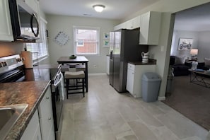 A kitchen with a stove, microwave, refrigerator, and a dining area with a table and chairs.
