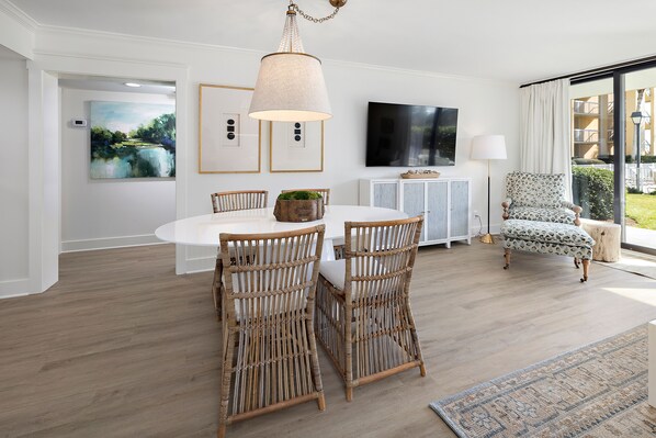 A dining area with a white table, two wicker chairs, a hanging light fixture, and a large window with a view of greenery. - Oceanfront King & Prince Villa w/ Access to Resort Amenities! (Saint Simons Island)