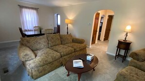 Ein Wohnzimmer mit einer Couch, einem Couchtisch, einer Lampe und einem Esstisch mit Stühlen.