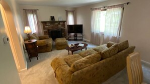 Ein Wohnzimmer mit Sofa, Sesseln, Couchtisch, Fernseher und Kamin.