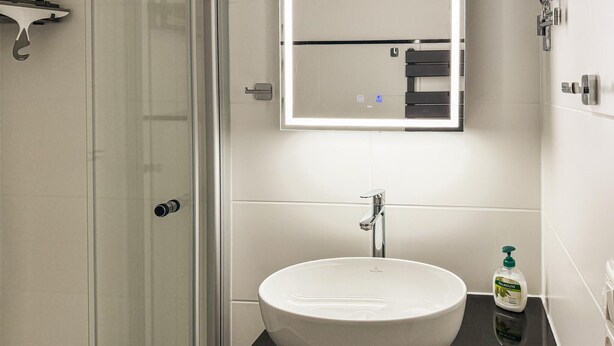 A bathroom with a white sink, a mirror, a shower, and a bottle of Palmolive soap. - Amazing apartment in Friedrichskoog with WiFi (Friedrichskoog)