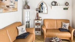 A living room with two tan leather sofas, a white cabinet with glass doors, a wooden side table with decorative items, a wall-mounted mirror, and a shelf with a clock and a sign. - Amazing apartment in Friedrichskoog with WiFi (Friedrichskoog)