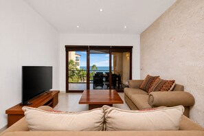 Een woonkamer met een flatscreen-tv, een bank, een salontafel en een balkon met uitzicht op zee.