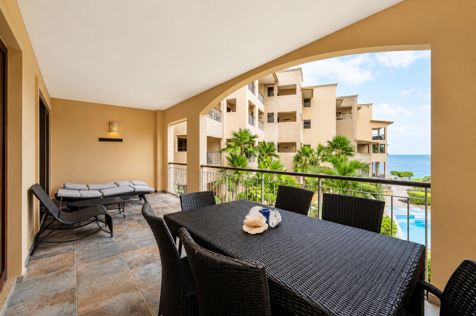 A balcony with a dining table and chairs, a sofa, and a view of a building and the ocean.