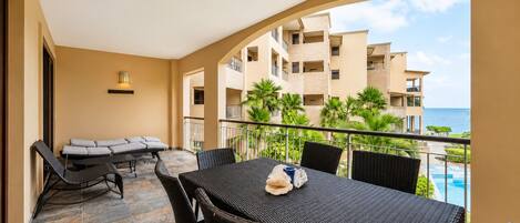 A balcony with a dining table and chairs, a sofa, and a view of a building and the ocean.