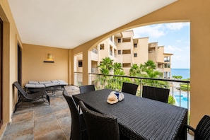 Un balcon avec une table et des chaises pour prendre les repas, un canapé et une vue sur un immeuble et l’océan.