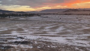 Ein weites, offenes Feld mit einem entfernten Gebirge und einem Sonnenuntergang im Hintergrund.