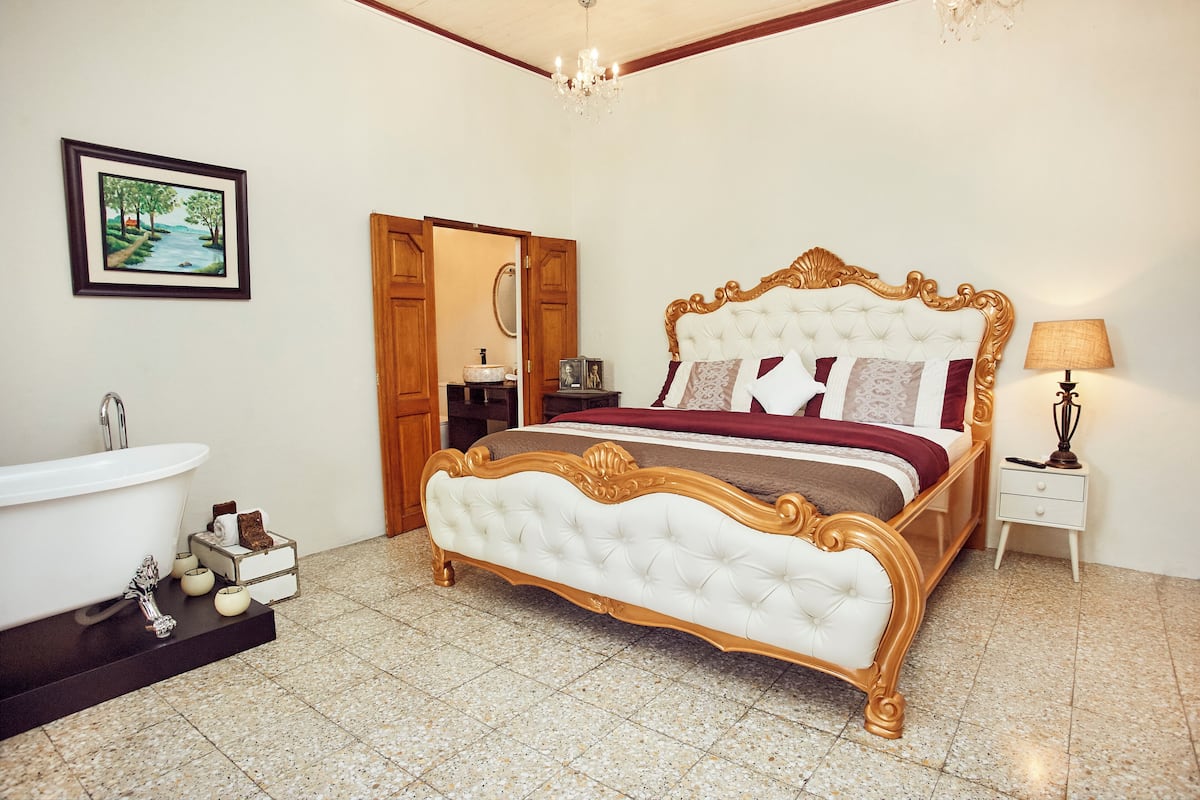 A bedroom with a large bed, a bathroom with a bathtub, and a painting on the wall.