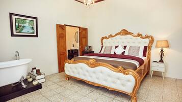 A bedroom with a large bed, a bathroom with a bathtub, and a painting on the wall.
