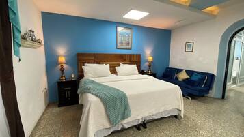Un dormitorio con una cama grande, dos mesitas de noche con lámparas, una pared azul y un cuadro de un paisaje urbano.