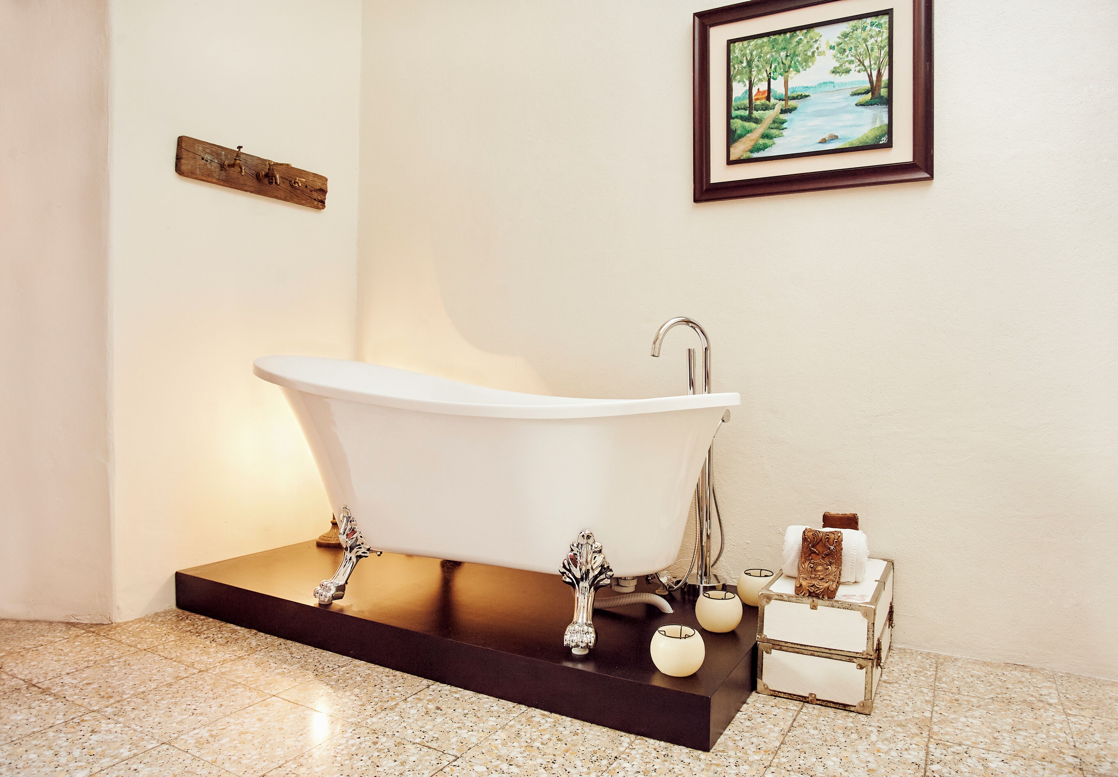 A freestanding bathtub in a bathroom with a framed painting above it and a wooden plaque on the wall.