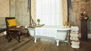 Ein Badezimmer im Vintage-Stil mit einer Badewanne auf Füßen, einer Holzbank mit gelber Sitzkissen, einem Schachbrett und einer Steinwand.