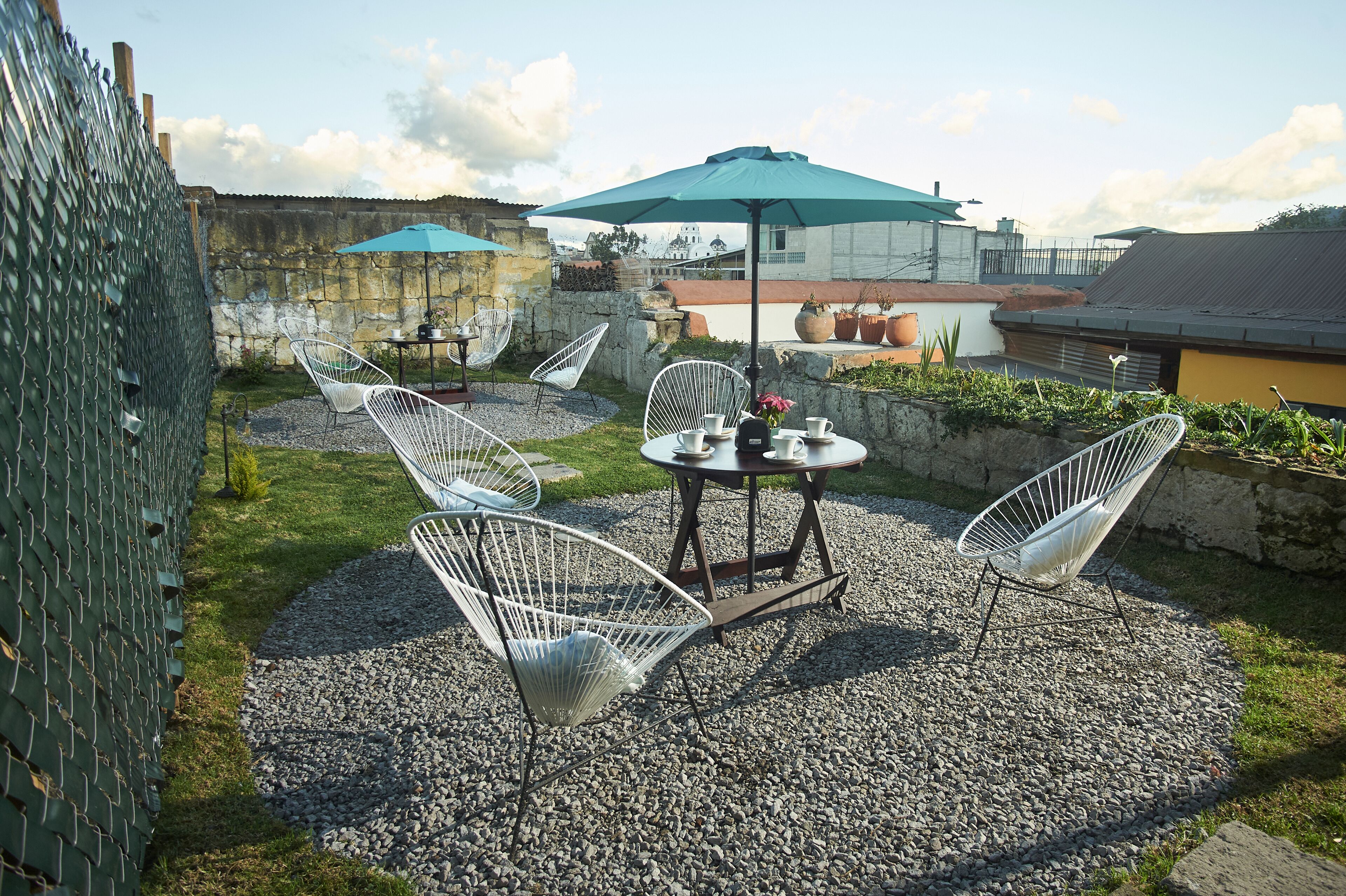 An outdoor patio with a table and chairs, a blue umbrella, and a stone wall.