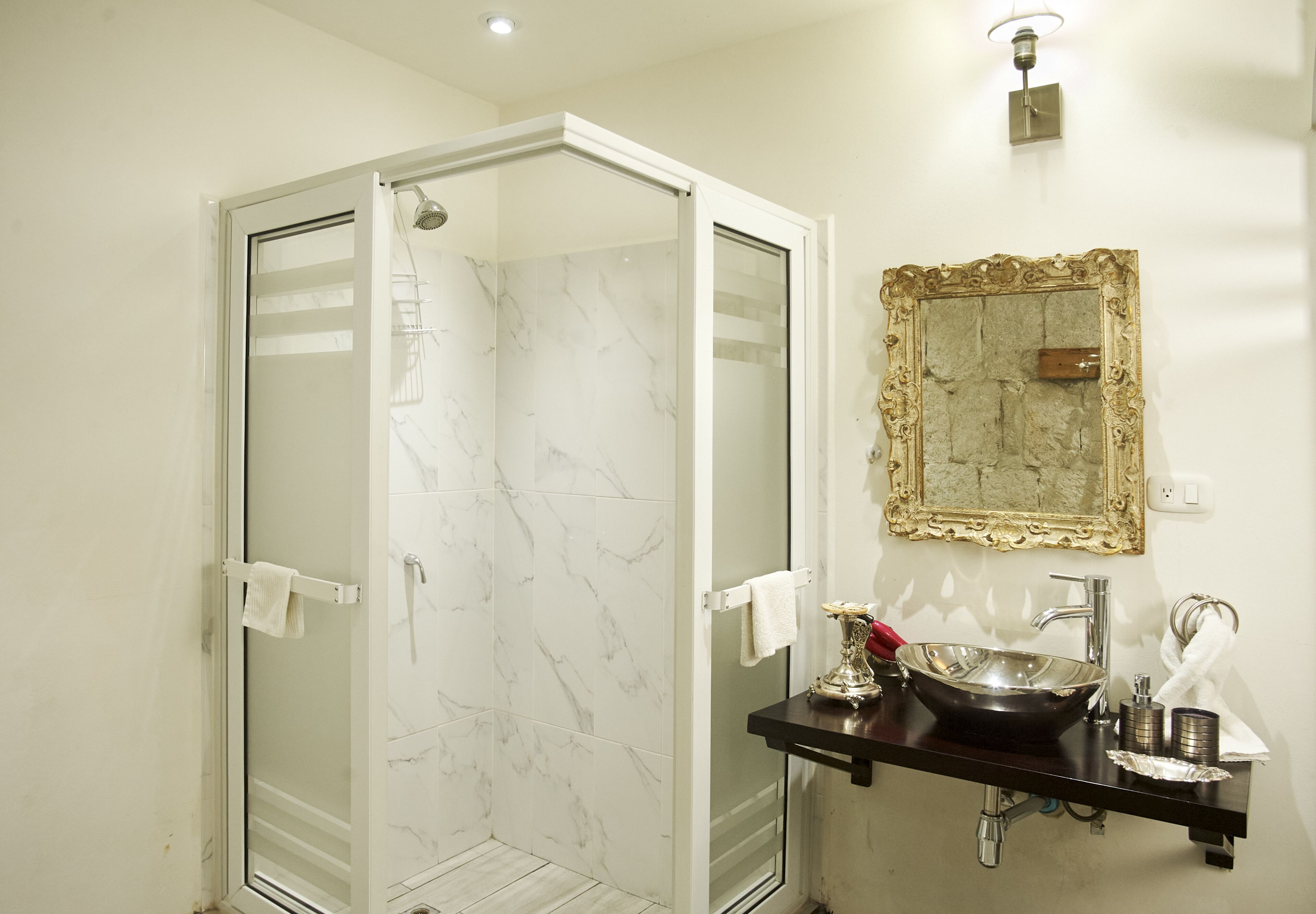A bathroom with a glass-enclosed shower, a marble-tiled wall, a sink with a vessel basin, and a decorative mirror.