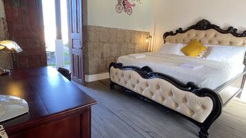 A bedroom with a wooden floor, a bed with a tufted headboard, a desk with a telephone, and a wall with a decorative sticker.