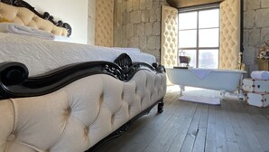 Ein Schlafzimmer mit einem großen Bett, einer Steinwand, einem Fenster und einer Badewanne.
