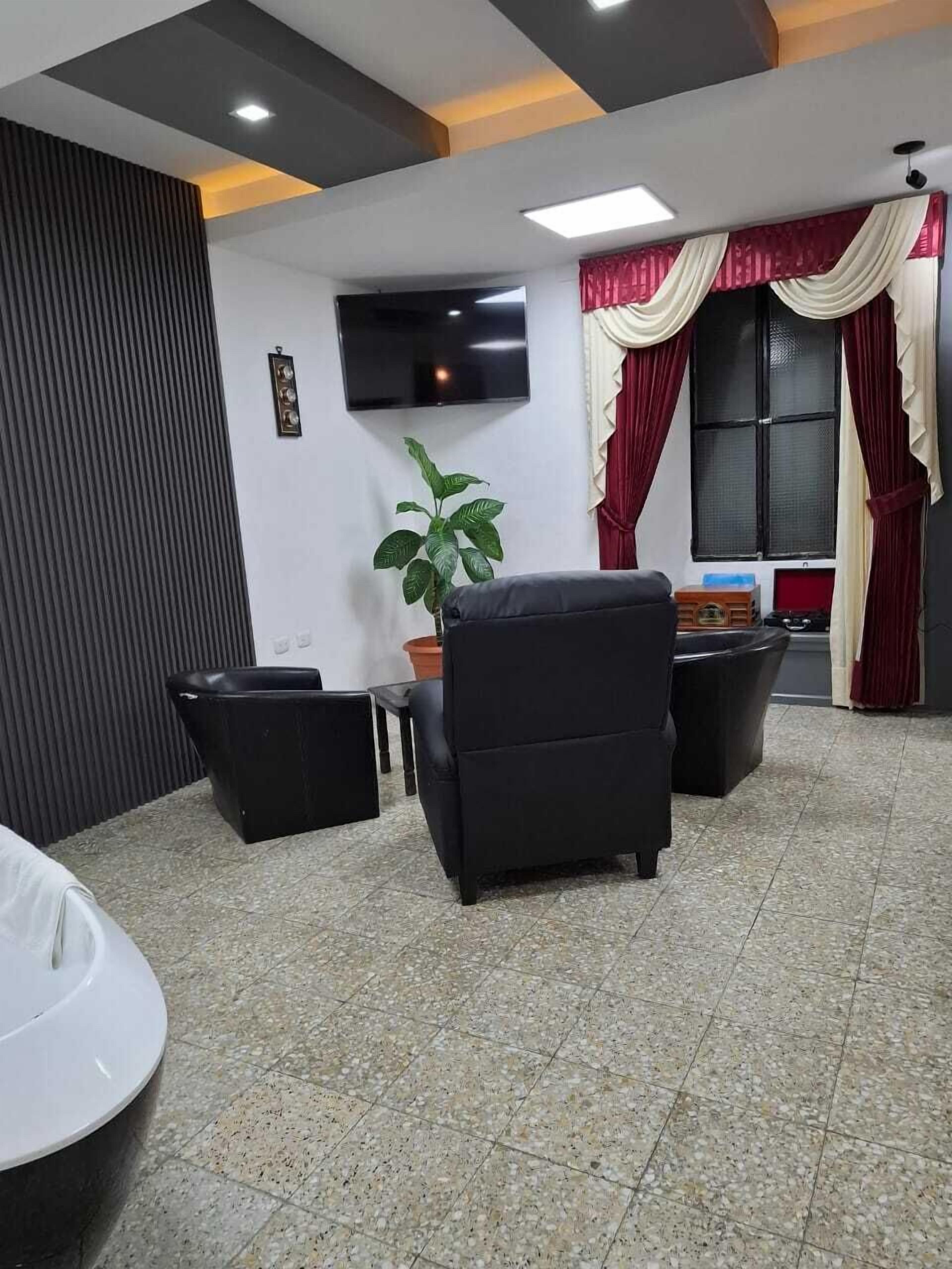 A modern living room with a flat-screen TV, a potted plant, and a black sofa.