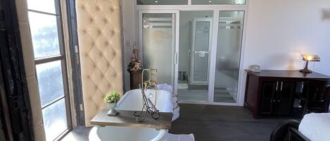 A room with a bathtub, a wooden table, a bed, and a wardrobe.
