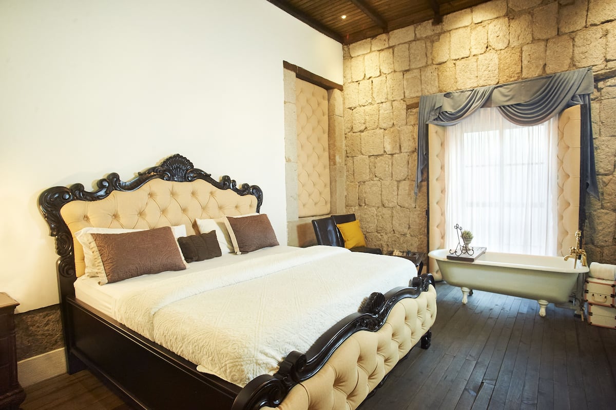 A bedroom with a large bed, a clawfoot bathtub, and a stone wall.