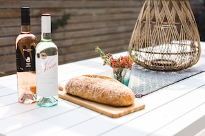 A table with a loaf of bread, two bottles of wine, and a wicker basket with flowers.