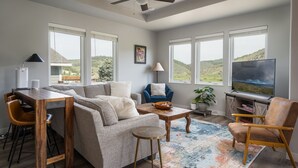 A living room with a sofa, coffee table, TV, and a ceiling fan. - Modern Home w/ Great Private Views, Hot Tub & Sauna (Tabernash)