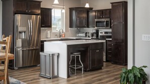 A modern kitchen with dark wood cabinets, stainless steel appliances, a central island with stools, and a view of the outdoors. - Modern Home w/ Great Private Views, Hot Tub & Sauna (Tabernash)