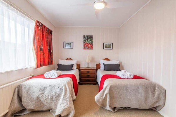 A twin room with two single beds, a nightstand, a ceiling fan, and a window with curtains.