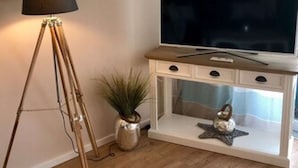 A living room with a wooden floor, a floor lamp, a television on a wooden console, and a potted plant. - Möwennest N°3 - Ground floor apartment with fantastic sun terrace and garden. (Grömitz)