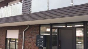 A modern building entrance with a glass door, a keypad entry system, and a brick facade. - Möwennest N°3 - Ground floor apartment with fantastic sun terrace and garden. (Grömitz)