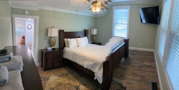 Un dormitorio con cama, mesitas de noche, lámpara, televisor, puerta y ventana.