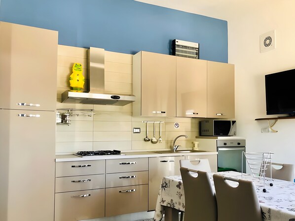 A modern kitchen with beige cabinets, a gas stove, a microwave, and a dining area with a table and chairs.