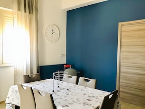 A dining area with a table set for two, a clock on the wall, and a blue accent wall.
