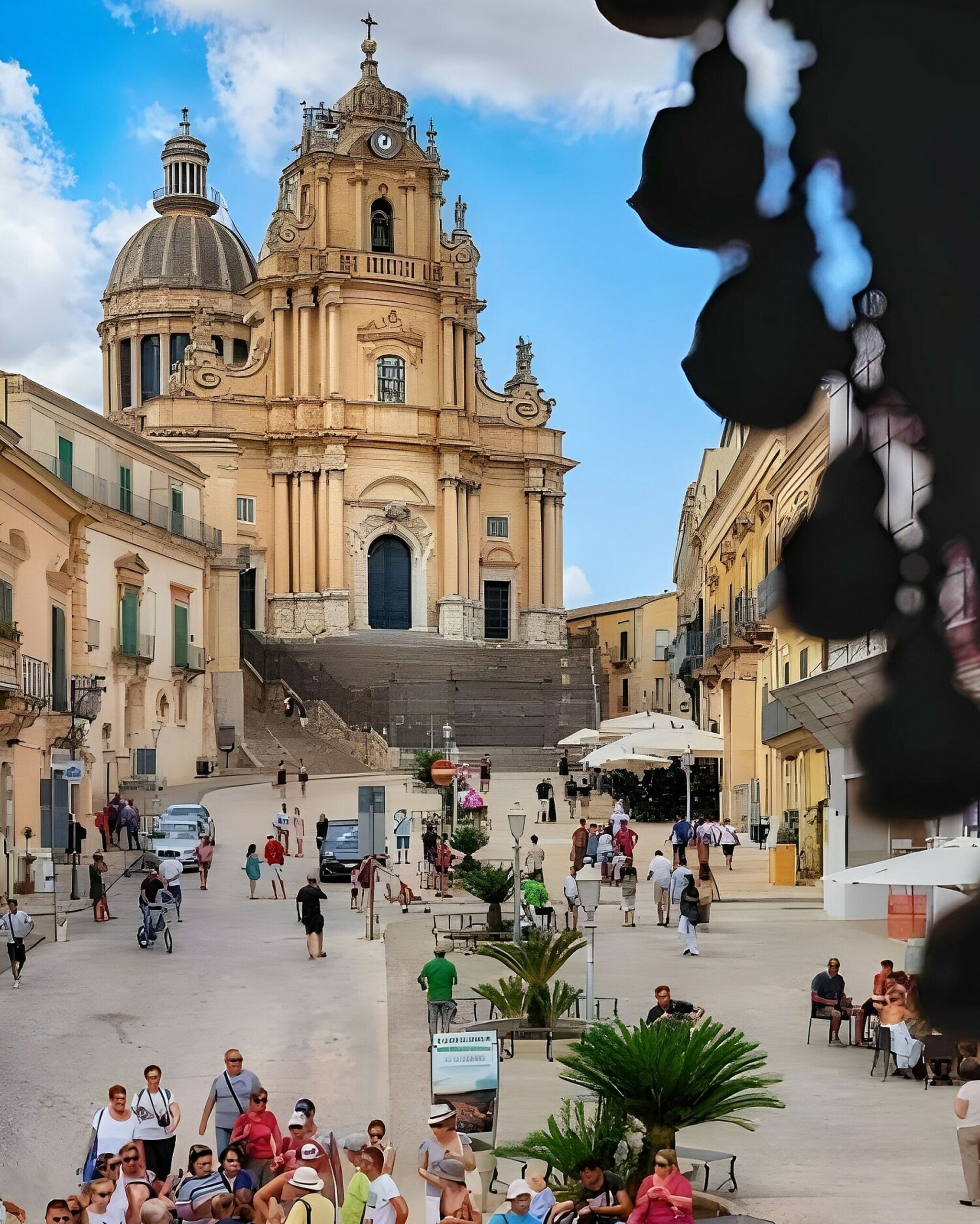 Um edifício histórico com cúpula e torre do sino, cercado por uma praça com pessoas e mesas ao ar livre.