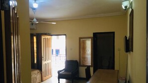 A room with a ceiling fan, a wooden door, a chair, and a small table. - Room-double Room With Balcony in the hea (Accra)