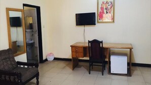 Una habitación con un escritorio de madera, una silla, un televisor montado en la pared y un espejo.