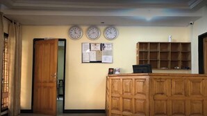 Un área de recepción con un mostrador de madera, tres relojes de pared y un tablón de anuncios con papeles.