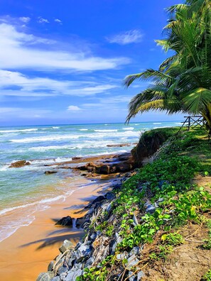 A beach with clear blue water, rocky shoreline, and lush greenery. - Room-double Room With Balcony in the hea (Accra)