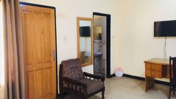 A room with a wooden door, a chair, a desk, a television, and a mirror.