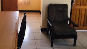 A room with a wooden table, a dark chair, a window with curtains, and a door. - Room-single Room With Balcony (Accra)