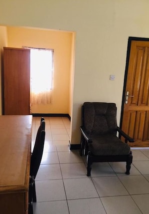 A room with a wooden table, a dark chair, a window with curtains, and a door. - Room-single Room With Balcony (Accra)