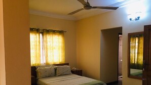 A bedroom with a bed, a nightstand, a ceiling fan, and a door leading to another room. - Room-single Room With Balcony (Accra)