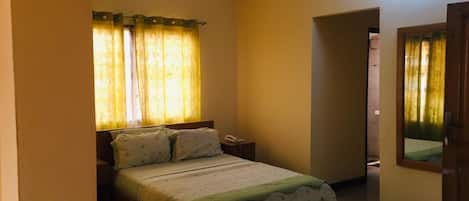 A bedroom with a bed, a nightstand, a ceiling fan, and a door leading to another room.