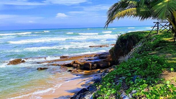 A beach with clear blue water, rocky shoreline, and lush greenery. - Room-single Room With Balcony (Accra)