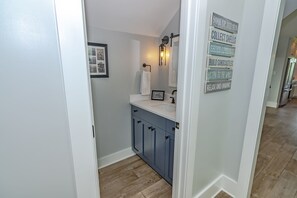 A bathroom with a white sink, blue cabinets, a framed picture, and a wall with motivational signs. - Large home with golf course view, open concept in living room with balcony (Bald Head Island)