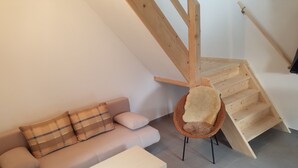 Et loftrum med en trappe i træ, en sofa med ternede puder og et hvidt sofabord.