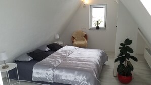 Et soveværelse med seng, stol, lampe og en potteplante.