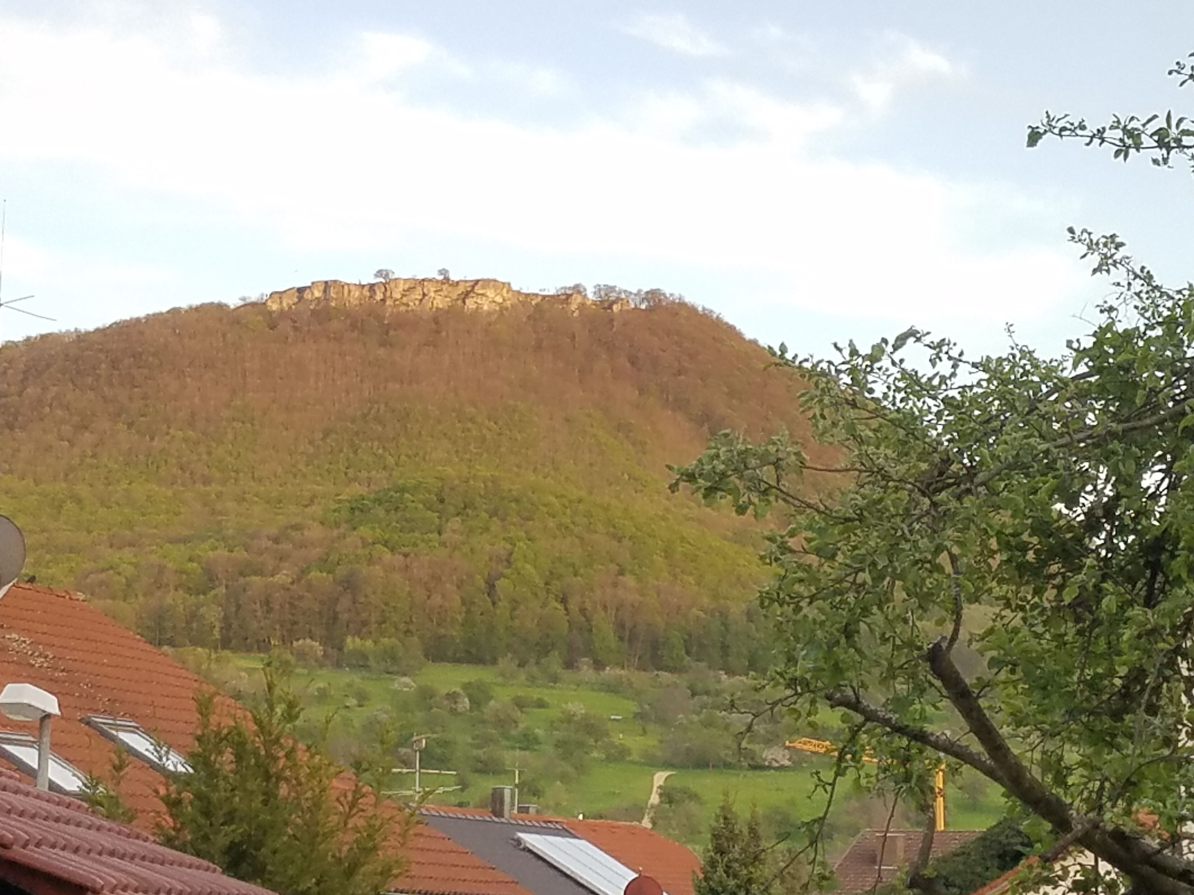 A view of a hill with a building on top, surrounded by greenery and a clear sky.