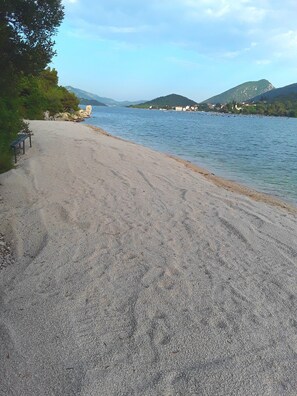 A beach with a bench and a rocky shoreline.