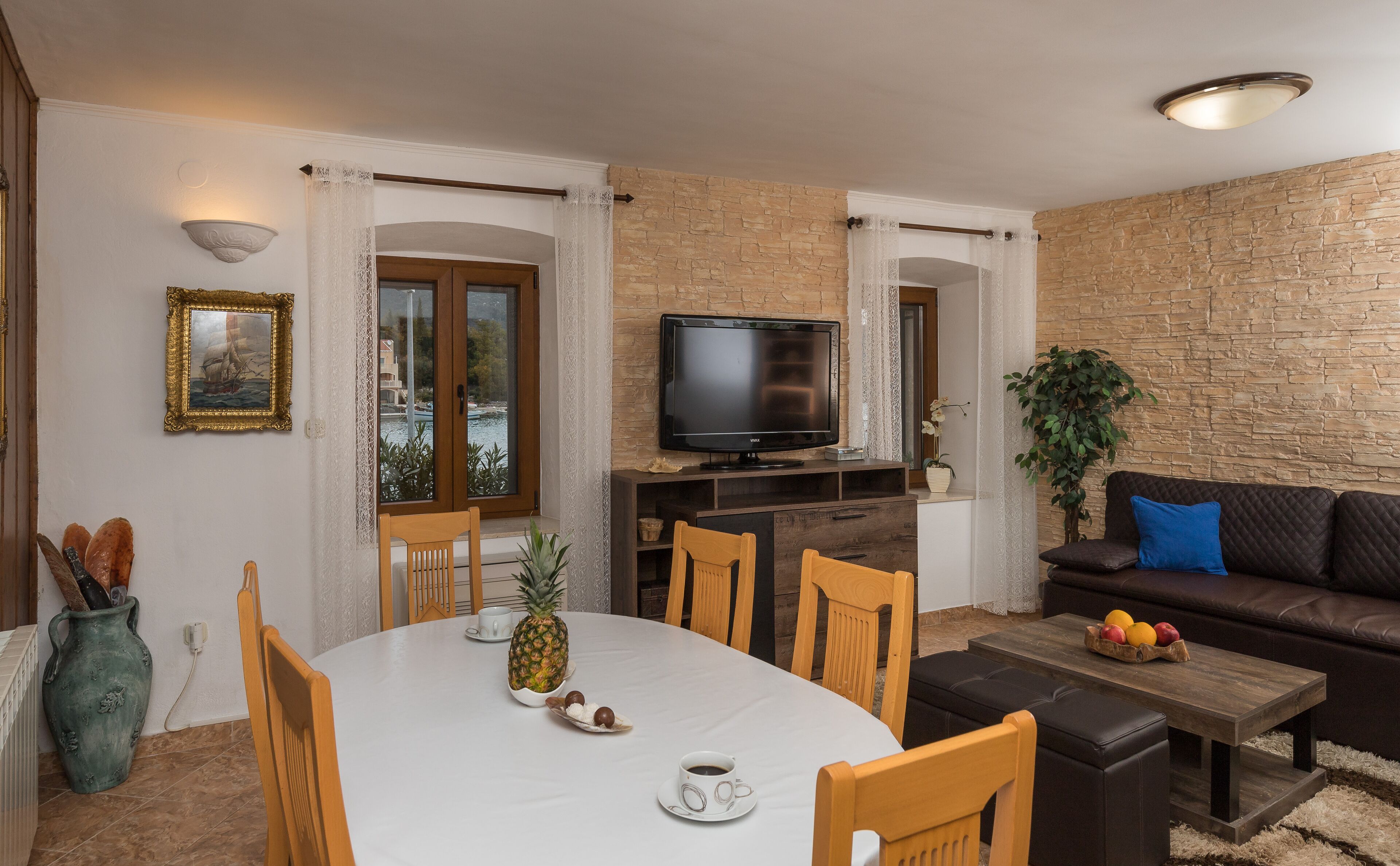 A dining area with a round table, chairs, a television, and a stone wall.
